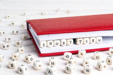 Phrase Short term written in wooden blocks in red notebook on white wooden table. Wooden abc. clipart