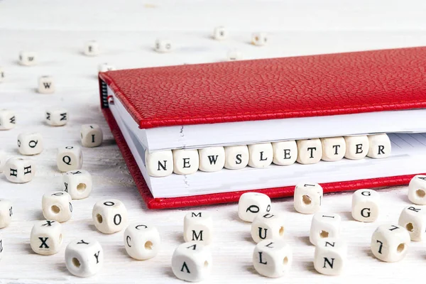 Word Newsletter written in wooden blocks in red notebook on white wooden table. Wooden abc.