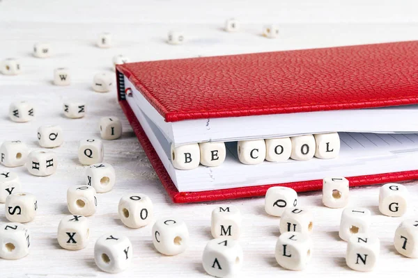 Phrase Be cool written in wooden blocks in red notebook on white wooden table. Wooden abc.