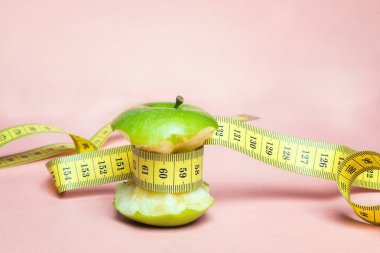 Yeşil elma güdük pembe arka plan sarı santimetre bant ile. Konsept spor, diyet, fitness, anoreksiya.