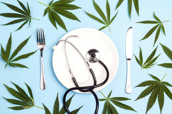 Medical concept table setting with cannabis and stethoscope on blue background.