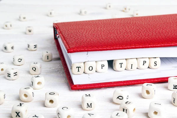 Phrase Top tips written in wooden blocks in red notebook on white wooden table. Wooden abc.