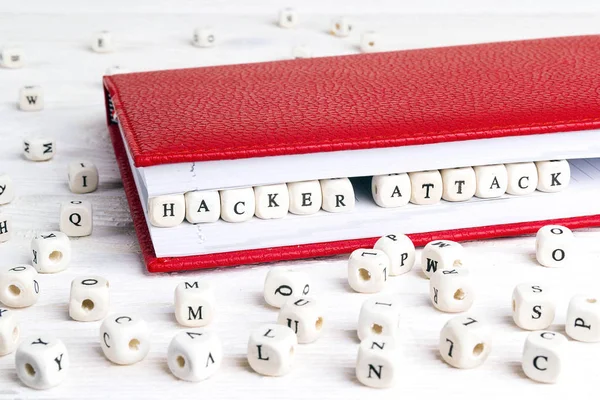 Phrase Hacker attack written in wooden blocks in red notebook on white wooden table. Wooden abc.