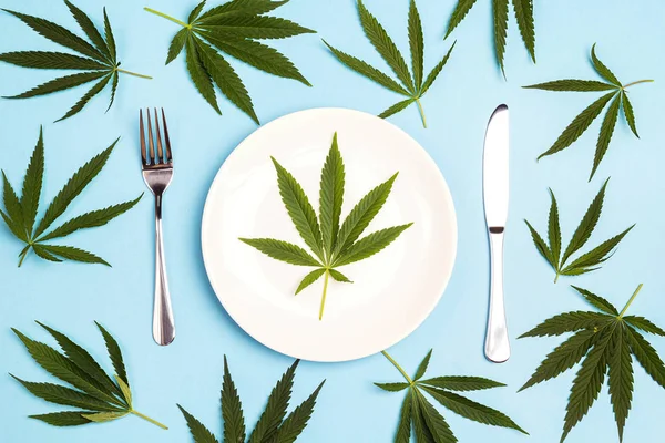 Medical concept table setting with cutlery and cannabis leaves on blue background. Top view.