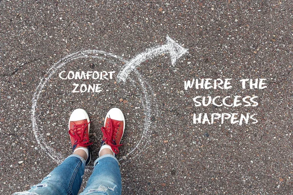 Exit from the comfort zone concept. Feet  in red sneakers standing inside circle comfort zone and outward arrow chalky on the asphalt.