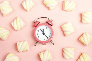 Pembe pembe bir arka plan üzerinde renkli sarmal marshmallow ile çalar saat. Düz yatıyordu, en iyi görünümü. 