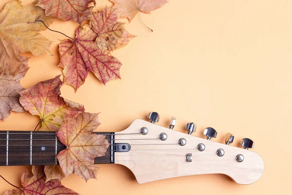 Electric guitar neck  with autumn maple leaves and copy space on yellow background. Melancholy music for autumn mood.