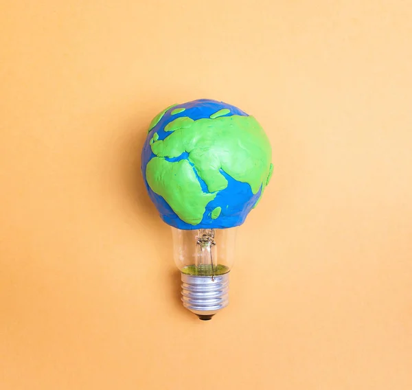 Light bulb with plasticine Earth planet model on yellow background. Global ecology, International Day of Energy Saving or Earth Hour concept.