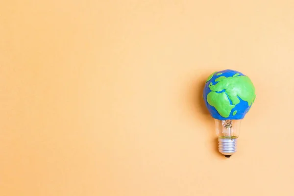 Light bulb with plasticine Earth planet model on yellow background with space for text. Global ecology, International Day of Energy Saving or Earth Hour concept.