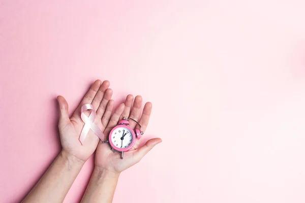 女の子の手がピンク乳がん啓発リボンと目覚まし時計を保持しています テキストやデザインの領域をコピーします 月月間キャンペーン — ストック写真