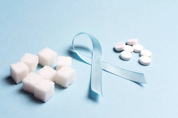 Blue ribbon rafine şeker ve hapları üzerinde mavi bir arka plan ile. Dünya Diyabet günü kavramı. Şeker şeker hastaları için alternatif.