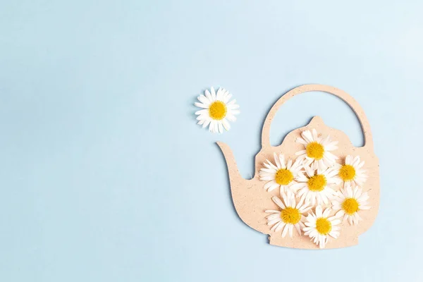 Teapot  symbol with chamomile flowers on a blue background. Chamomile come out of the teapot spout like steam. Chamomile tea concept. Flat lay, top view.