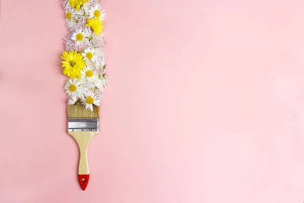 Paint brush drawing with flowers on a pink background wiyh copy space. Fresh flowers instead of paint. Flat lay.