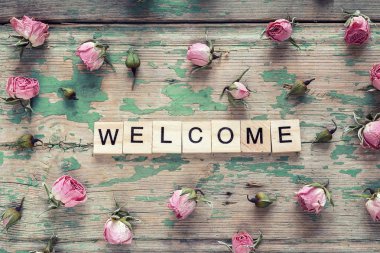 Hoş geldiniz işareti ve eski ahşap arka plan üzerinde küçük pembe Gül. 