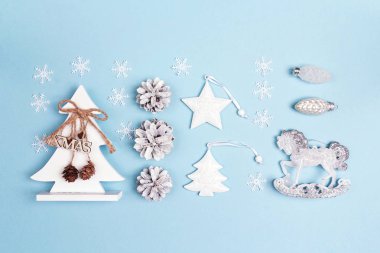 Mavi zemin üzerine beyaz Noel süsleri kümesi. Çam ağaçları, koniler, kar taneleri, sallanan at ve diğer baubles. Yukarıdan aşağıya Noel kompozisyon.