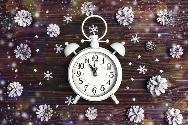 Christmas alarm clock with snow painted pine cones on wooden background. Christmas timer. Time to celebrate.