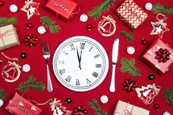 Festive table setting with dish clock and Christmas decorations on red cloth background. Top view. Christmas tableware.