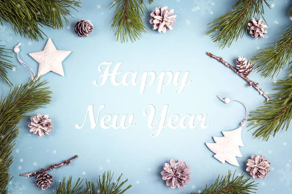 New year greeting message with fir branches and white decorations on the blue background. Top view.