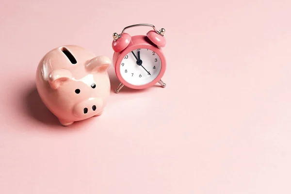 Piggy bank and classic alarm clock on pink background. Time to saving, money, banking concept.  Flat design, copy space for text.