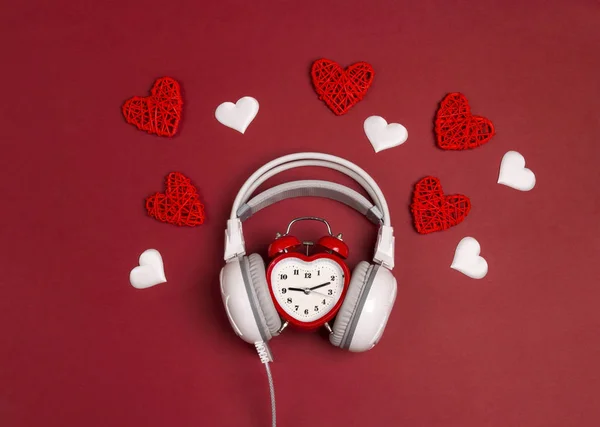 Białe słuchawki z budzik i serca na czerwonym tle. — Zdjęcie stockowe