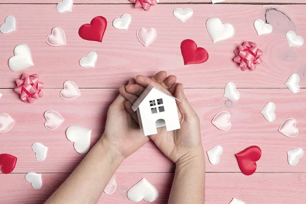 Las manos de las mujeres con miniatura casa de juguete blanco con corazones en rosa — Foto de Stock