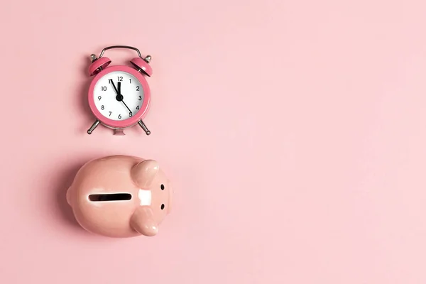 Piggy bank and classic alarm clock on pink background. Time to s