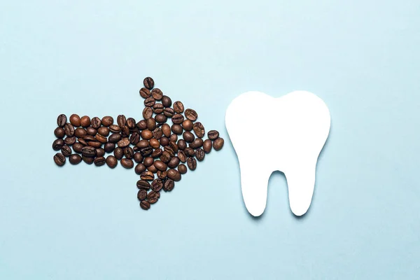 Tooth and coffee bean arrow on a blue background. Coffee spoils