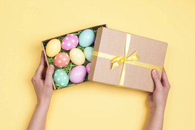 Sarı arka plan üzerinde hediye kutusu ile Paskalya yumurta kadın el ele tutuşur