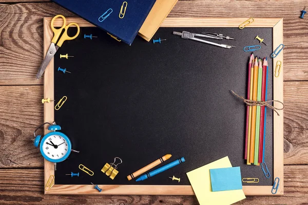 A chalkboard with school supplies and alarm clock on a rustic wo — Stock Photo, Image