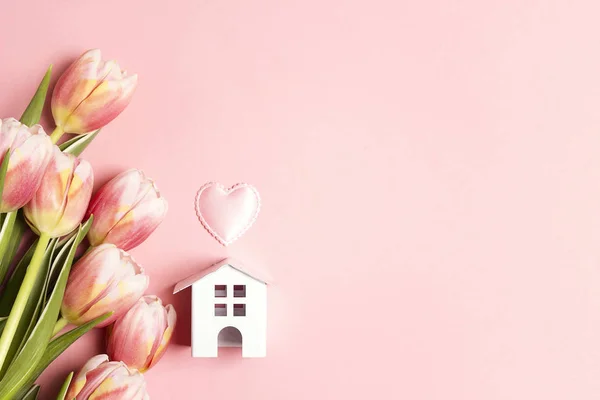 Casa de brinquedo branco em miniatura com flores de tulipa no fundo rosa — Fotografia de Stock