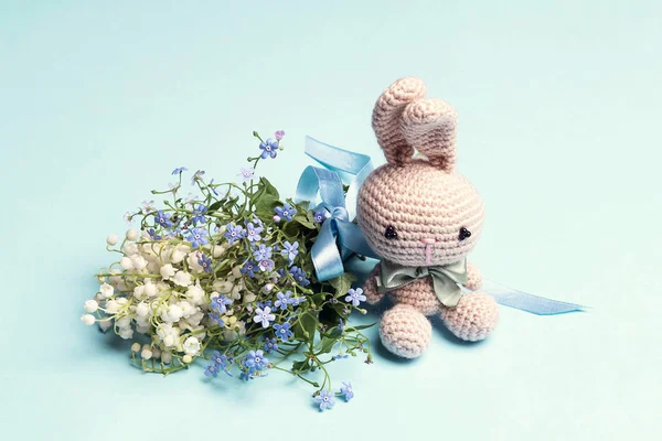 Cute toy bunny with bouquet of lily of the valley and forget-me-
