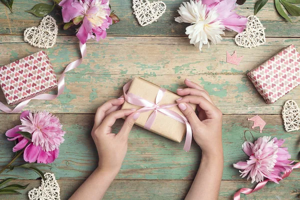 Le mani delle donne stanno avvolgendo un regalo circondato da peonie su un wor — Foto Stock