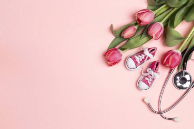 Pembe bac üzerinde stetoskop ve bebek kız ayakkabıları ile lale Demet