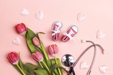 Pembe bac üzerinde stetoskop ve bebek kız ayakkabıları ile lale Demet