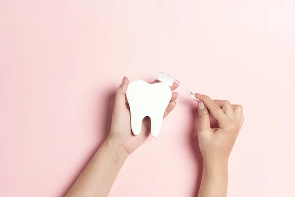 Женские руки с символом зуба и зубной щеткой на розовом фоне — стоковое фото