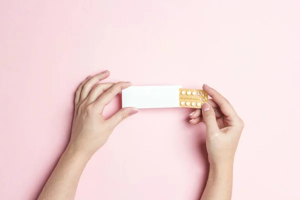 Female hands holding birth control pills on pink background. Wom