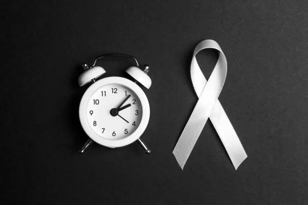 White lung cancer awareness ribbon and alarm clock on black back