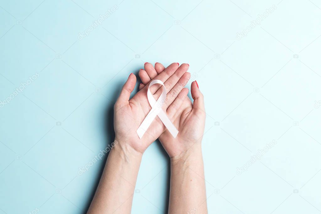 Female hands holding white ribbon on a blue background. 
