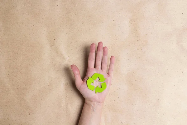 Female hands hold a recycles eco symbol on brown paper backgroun — Stock Photo, Image
