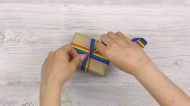 Dişi eller, açık ahşap bir masa üzerinde gökkuşağı LGBT kurdelesiyle bir hediye paketler. Homoseksüel ve lgbt kavramı.