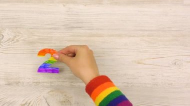 Kadın eli, masa üstüne koyuyor. Gökkuşağı renkli figürler. Ahşap arka planda 2020. Haziran ayında LGBT Gurur Ayı.