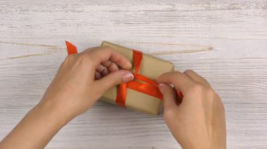 Kadın eli, üzerinde kırmızı kurdele olan bir hediyeyi açık tahta masaya koyar. Tatil kompozisyonu.