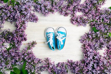 Açık ahşap arka planda leylak çiçekli şirin pembe erkek çocuk ayakkabıları.. 