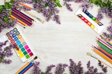 Çalışma alanı çerçevesi suluboya, fırçalar, kalemler ve ahşap arka planda leylak çiçekleri. Düz konum, üst görünüm, kopyalama alanı.