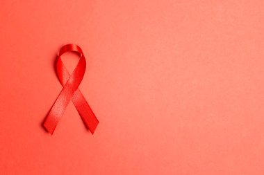 Kırmızı arkaplanda AIDS farkındalığının sembolü olarak kırmızı kurdele ve metin için kopyalama alanı. 1 Aralık Dünya Yardım Günü konsepti.