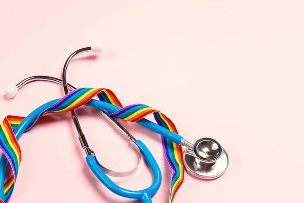 Stethoscope with LGBT rainbow ribbon on pink background. Medical support LGBT community. Copy space for text.