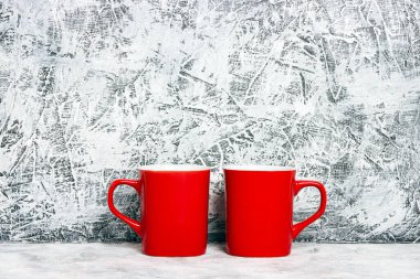 Gri alçı bir duvara karşı iki kırmızı kahve fincanı. Metin veya tasarım için yer.
