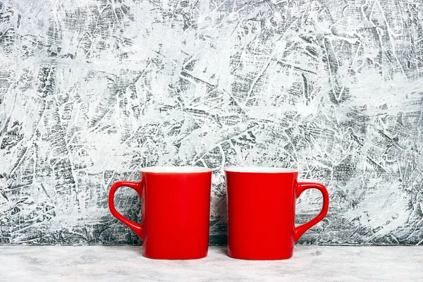 Gri alçı bir duvara karşı iki kırmızı kahve fincanı. Metin veya tasarım için yer.