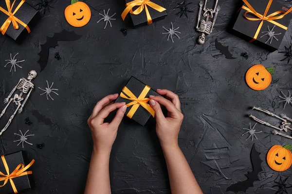 Female hands decorate a Halloween gift surrounded by boxes and decorations on a black background. Festive set with funny pumpkins, bats, skeletons and spiders. — Stock Image Female Hands Decorate Halloween Gift Surrounded Boxes Decorations Black Background Stock Photo