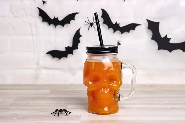 Orange Halloween cocktail in skull glass jars with cobwebs and bats. Copy space for text.
